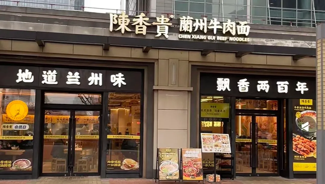 The storefront of a Chen Xianggui Lanzhou noodle shop with its red signage