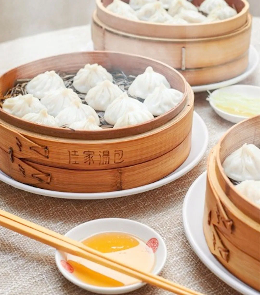 Soup dumplings in bamboo steamers branded 佳家汤包, with a spoon and chopsticks
