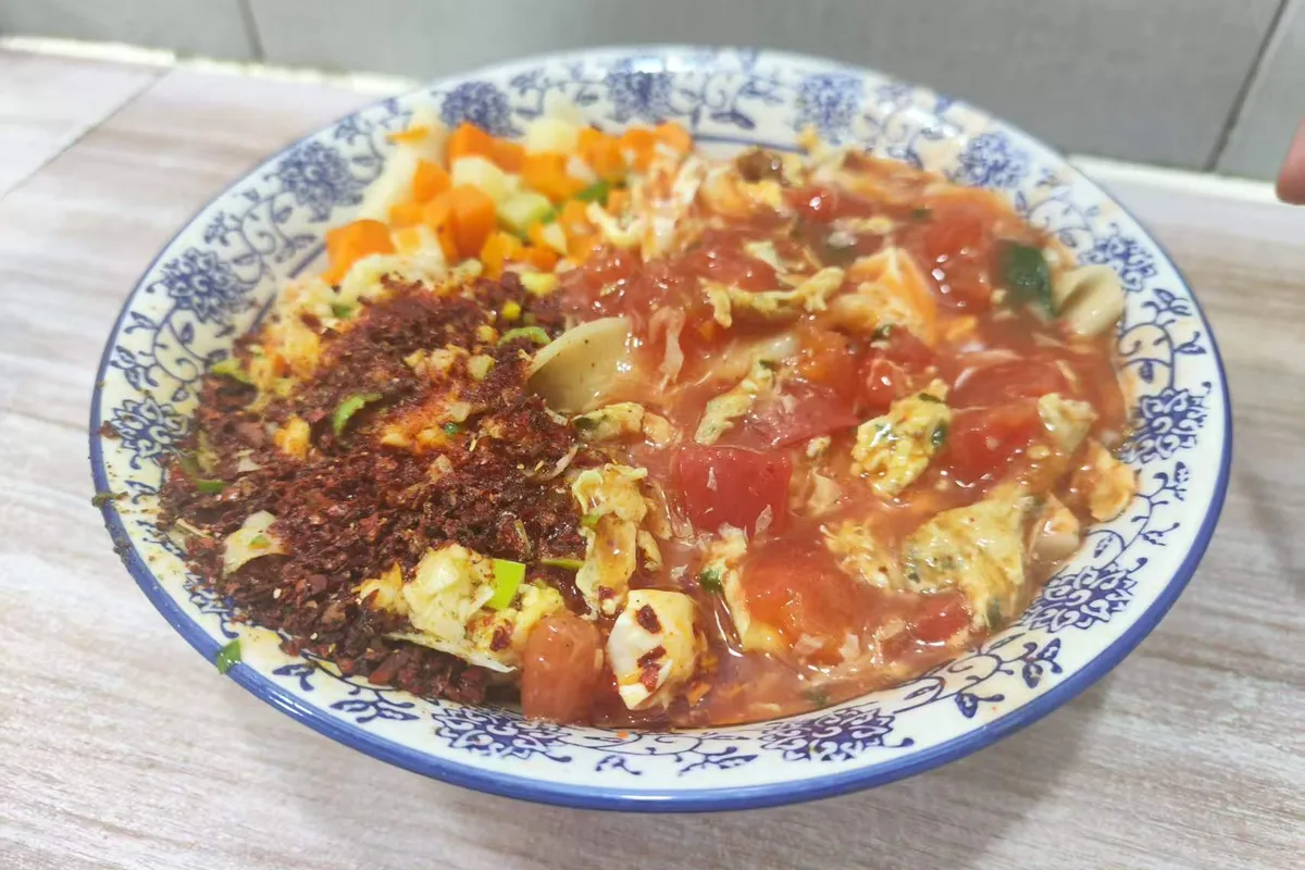 A bowl of three-in-one oil-splashed noodles in a blue-and-white ceramic bowl — hand-pulled stick noodles under chili oil, topped with tomato-and-egg and vegetable mince