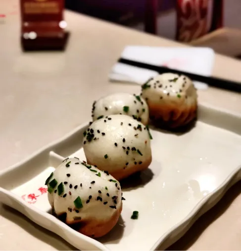 Four shengjian bao on a plate — pillowy white tops, golden pan-fried bottoms