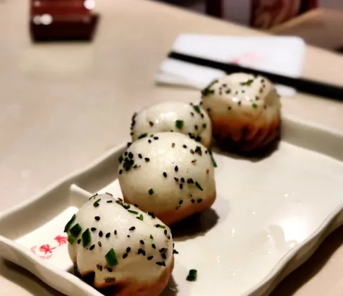 Four shengjian bao on a plate — pillowy white tops, golden pan-fried bottoms
