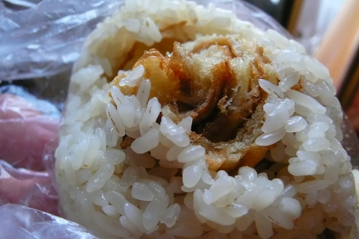 A sticky rice ball cut open to show a strip of crisp youtiao and pork floss inside the white glutinous rice, still wrapped in clear plastic