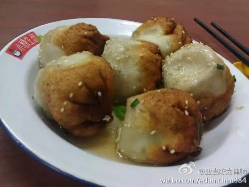 A plate of pan-fried shengjian fresh from the pan, golden crisp bottoms up